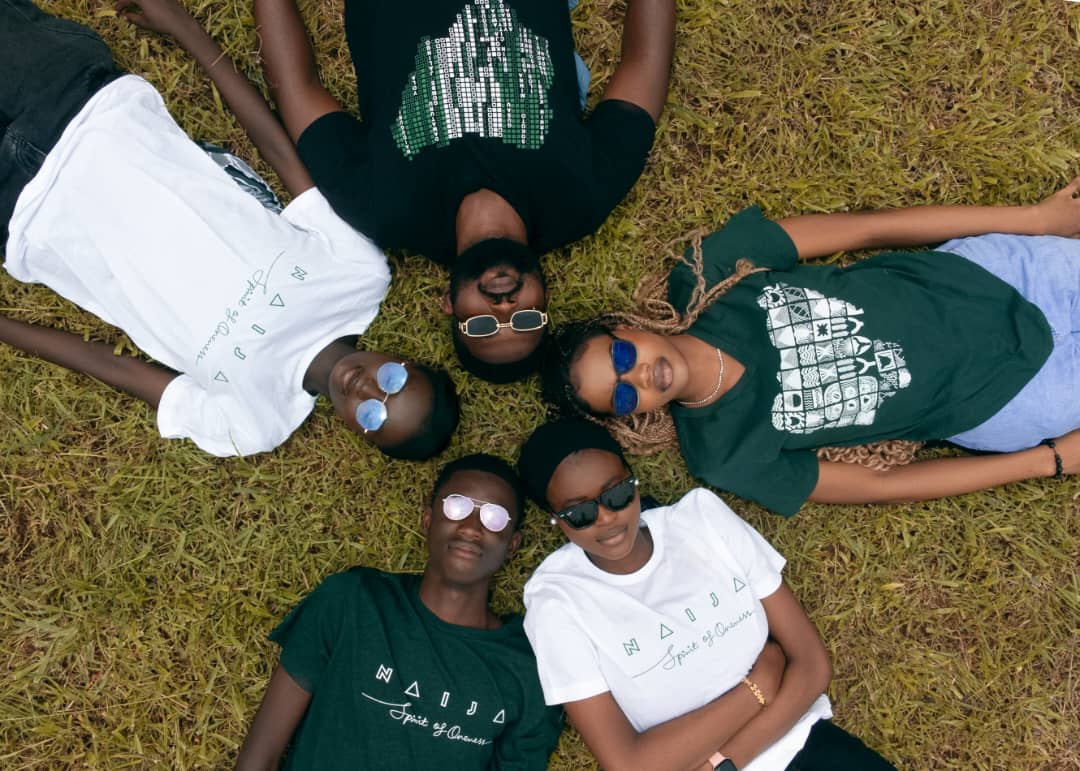 Individuals wearing AREWATEES printed shirts whilst laying in a circle, with the crown of their heads touching each other.